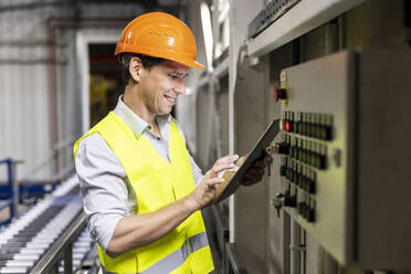 Smiling worker using tablet PC by control panel in warehouse - PESF03810