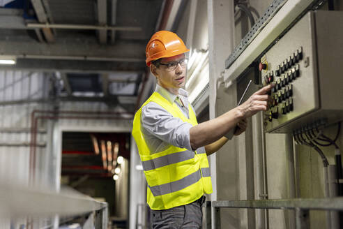 Arbeiter mit Tablet-PC, der den Druckknopf einer Steuertafel in der Industrie drückt - PESF03811