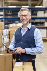 Happy mature manager with tablet PC standing in warehouse - PESF03838