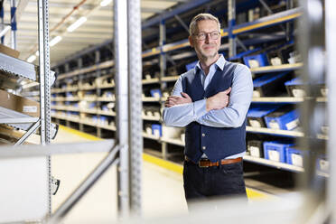 Smiling manager standing with arms crossed in warehouse - PESF03841
