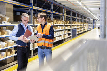 Worker discussing over tablet PC with manager standing in aisle at warehouse - PESF03847