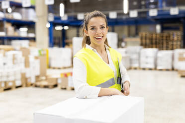 Happy worker with tablet PC leaning on box in warehouse - PESF03859