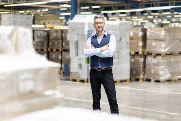 Smiling manager standing with arms crossed in warehouse - PESF03862