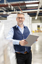 Manager wearing eyeglasses standing with tablet PC by box in warehouse - PESF03868