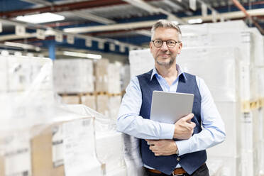 Lächelnder Manager mit Brille, der mit einem Tablet-PC neben einer Kiste im Lager steht - PESF03869