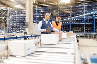 Manager discussing over cardboard boxes with colleague by conveyor belt in warehouse - PESF03897