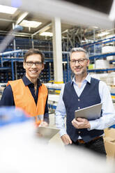 Smiling manager standing with hand in pocket by colleague in warehouse - PESF03899