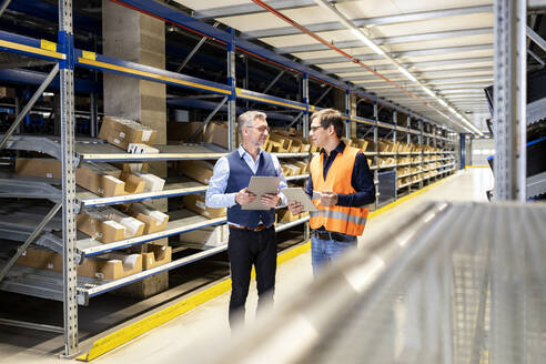 Manager discussing with worker standing in aisle at warehouse - PESF03900