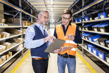 Manager discussing over tablet PC with worker in aisle at warehouse - PESF03901