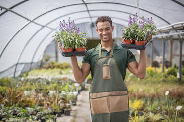 Porträt lächelnder männlicher Mitarbeiter einer Gärtnerei mit Blumen im Gewächshaus - CAIF32585