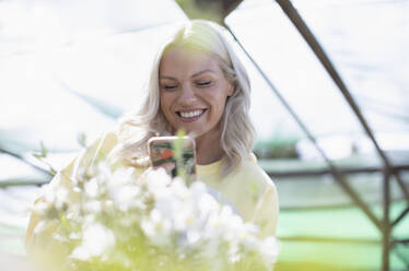 Glückliche Frau mit Smartphone beim Fotografieren von Blumen - CAIF32592