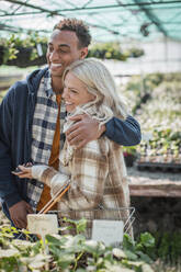 Glückliches Paar, das sich umarmt und in einem Gartengeschäft einkauft - CAIF32595