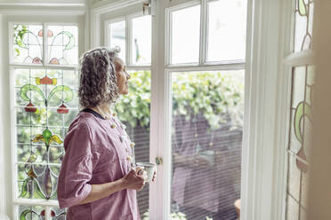 Happy senior woman with tea at window - CAIF32623