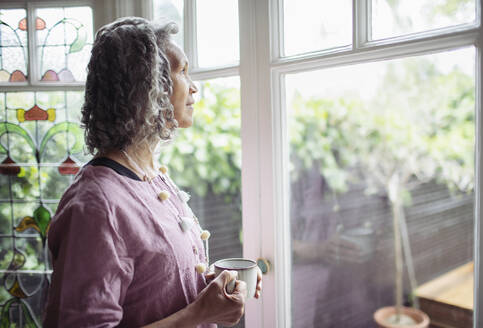 Nachdenkliche ältere Frau trinkt Tee am Fenster - CAIF32639