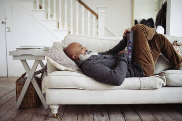 Mature man relaxing on living room sofa with digital tablet - CAIF32640