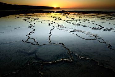 Gefrorene eisige Wasser des Flusses mit Rissen bei Sonnenuntergang Zeit in Küstengebiet mit Berg gegen wolkenlosen Himmel in der Natur - ADSF34766