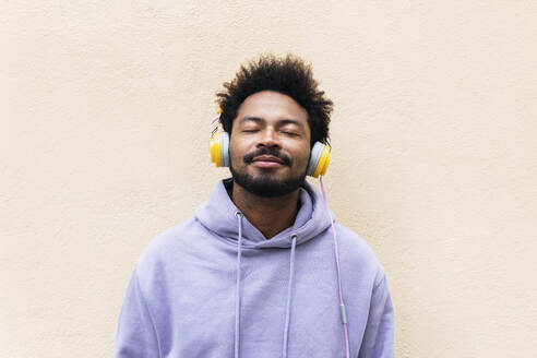 Mann genießt Musik über Kopfhörer vor einer cremefarbenen Wand - PNAF03834