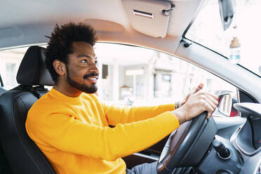 Smiling Afro man wearing yellow t-shirt driving car - PNAF03859