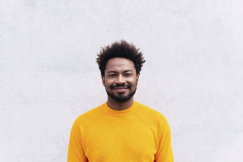 Lächelnder Afro-Mann vor einer weißen Wand stehend - PNAF03873