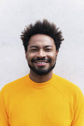 Happy Afro man wearing yellow t-shirt in front of white wall - PNAF03876