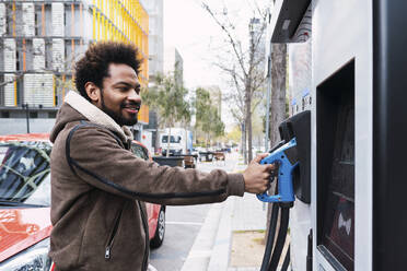 Afro-Mann hält elektrische Pumpe an Ladestation - PNAF03878