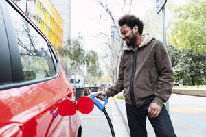 Glücklicher Mann, der sein Elektroauto an einer Tankstelle auflädt - PNAF03879