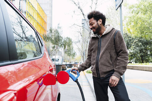 Glücklicher Mann, der sein Elektroauto an einer Tankstelle auflädt - PNAF03879