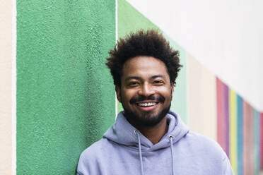 Lächelnder Afro-Mann, der sich an eine bunte Wand lehnt - PNAF03883