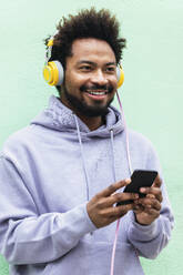 Smiling man holding mobile phone listening music through headphones - PNAF03888