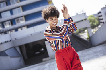 Happy woman with Afro hairstyle clapping hands at parking deck - UUF26183