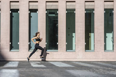 Junge Frau joggt auf dem Fußweg am Gebäude - JSRF02012