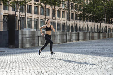 Frau in Sportkleidung joggt auf dem Fußweg - JSRF02015