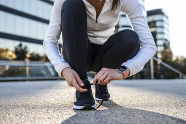 Hands of woman tying shoelace on footpath - JSRF02027