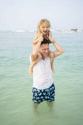Vater, der seine Tochter auf den Schultern trägt, steht im Meer am Strand - SVKF00182