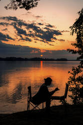 Silhouette Frau malt am See bei Sonnenuntergang - LLUF00539