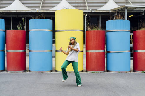 Junge Frau mit Kopftuch tanzt vor einem Betonrohr - MEUF05705