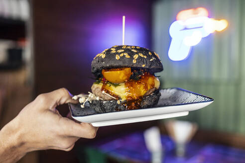 Hands of woman holding black burger on plate at restaurant - JSRF02054