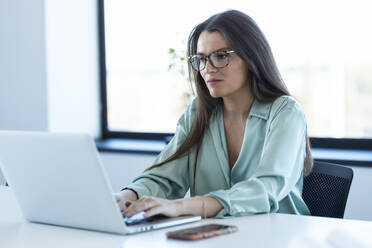 Businesswoman working on laptop with concentration at office - JSRF02071