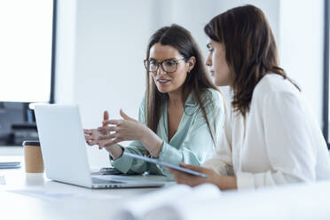 Businesswomen looking at laptop discussing with colleague in office - JSRF02082