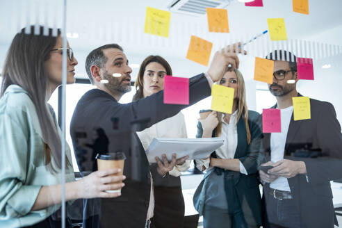 Businessman explaining colleagues over adhesive notes in meeting at office - JSRF02086