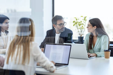 Businesswomen and businessman discussing in board room at office - JSRF02093