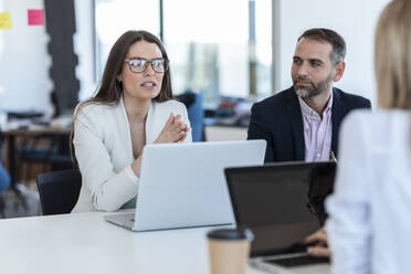 Businesswoman wearing eyeglasses discussing strategy with colleagues in office - JSRF02095