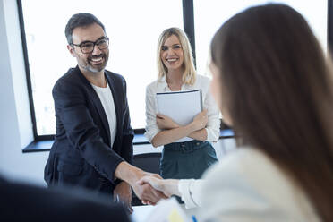 Happy businessman greeting businesswoman in office - JSRF02099