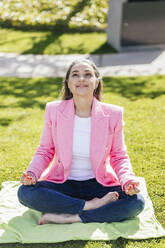 Smiling businesswoman looking up sitting cross-legged in office park on sunny day - IFRF01670