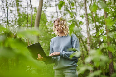 Freiberufler mit Laptop inmitten von Bäumen im Wald - MMIF00309