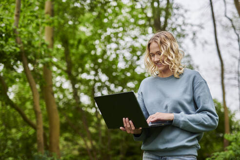 Happy freelancer working on laptop in forest - MMIF00311