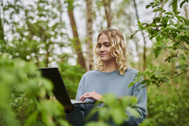 Lächelnder Freiberufler bei der Arbeit am Laptop im Wald - MMIF00315