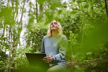 Junger Freiberufler, der sich in der Natur entspannt und einen Laptop benutzt - MMIF00319