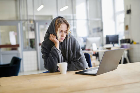 Junge Frau in gemütlicher Loungewear sitzt am Schreibtisch im Büro mit Laptop - MMIF00333