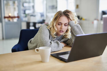 Tired young woman sitting at desk in office with laptop - MMIF00338